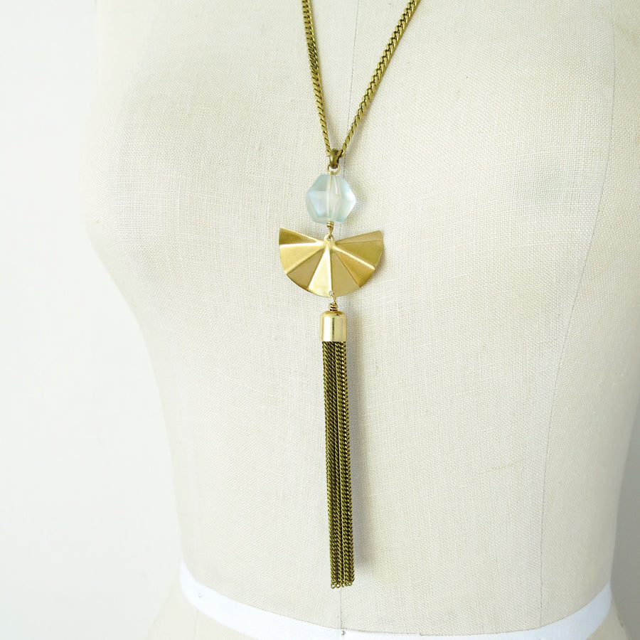Close up on pendant of Concertina Necklace. Made of acrylic bead with brass charm and tassel.