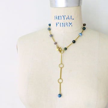 Resilience Necklace by MoonRox can be worn as a lariat or a necklace. Semi-precious stones are spaced along brass components. This photo shows the necklace as a lariat in kyanite.