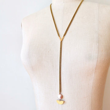 Sail Away With Me Lariat is a Y-style chain necklace with lustrous coin-shaped freshwater pearl and brass semi-circle detail